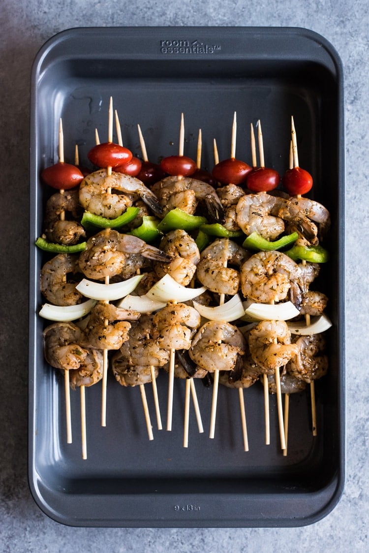 Shrimp skewers in a large baking dish waiting to be grilled.