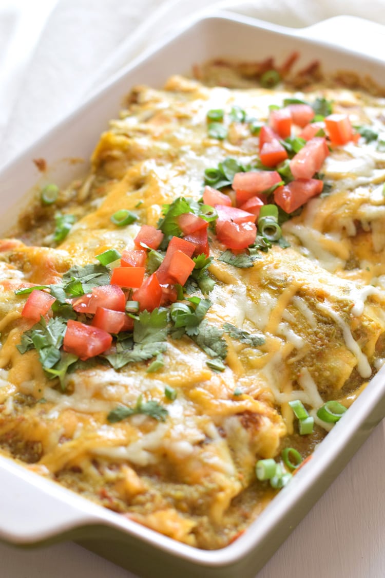 Enchiladas Verdes in a baking dish covered in salsa verde and shredded cheese.