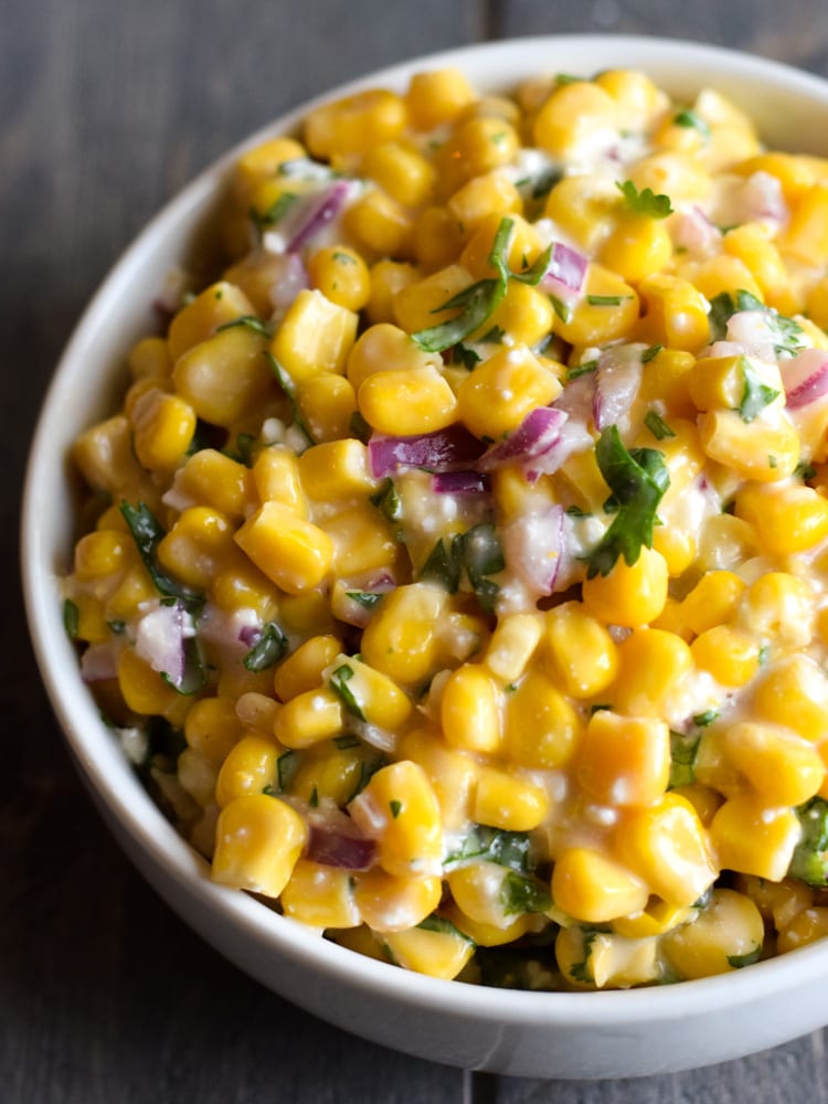 A bowl filled with mexican street corn made from yellow kernel corn, mayo, cotija cheese, red onions and cilantro.