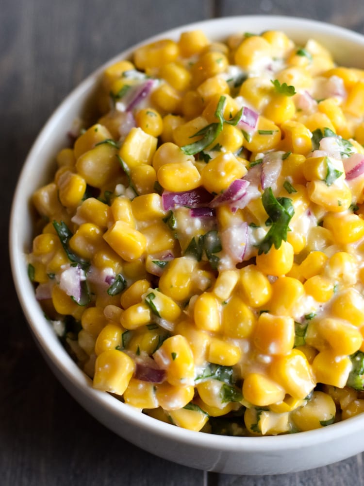 Un tazón lleno de maíz callejero mexicano hecho de maíz de grano amarillo, mayonesa, queso cotija, cebollas rojas y cilantro.