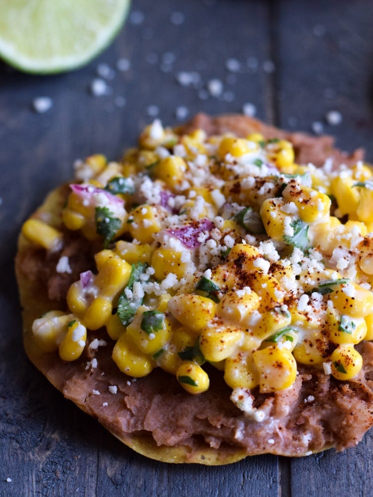 een tostada overgoten met geroosterde bonen, Mexicaanse straatmaïs en cotija kaas.