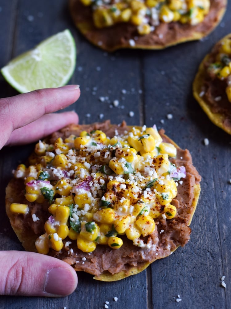 A hand grabbing a mexican street corn tostada.