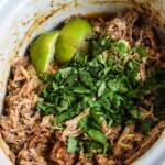 Chicken Carnitas in a slow cooker topped with cilantro.