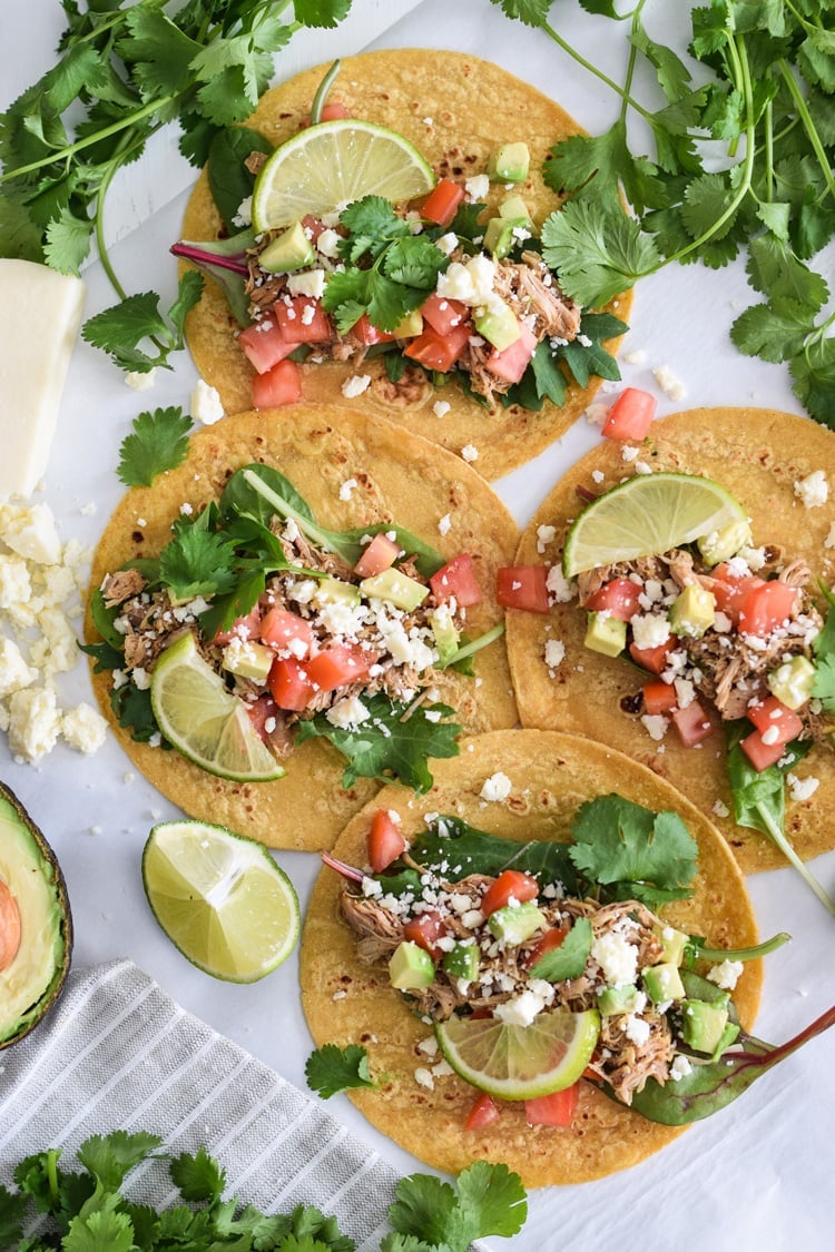 Four tacos filled with chicken carnitas and taco toppings.