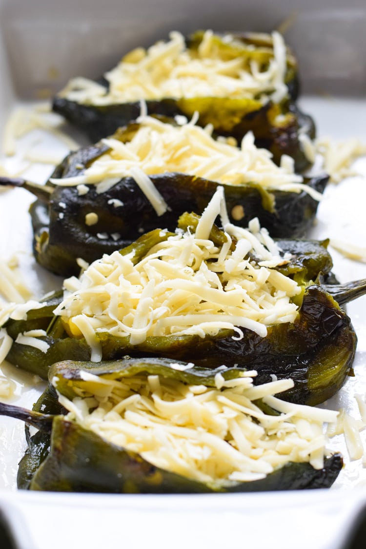 Roasted poblanos stuffed with shredded cheese in a baking dish.