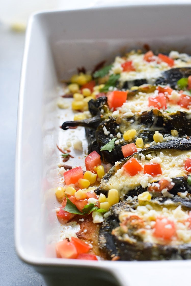 Baked chile rellenos in a baking dish topped with corn and diced tomatoes.