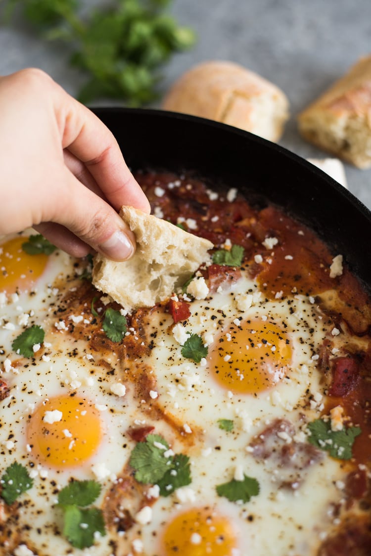 Bread being dipped into shakshuka with feta