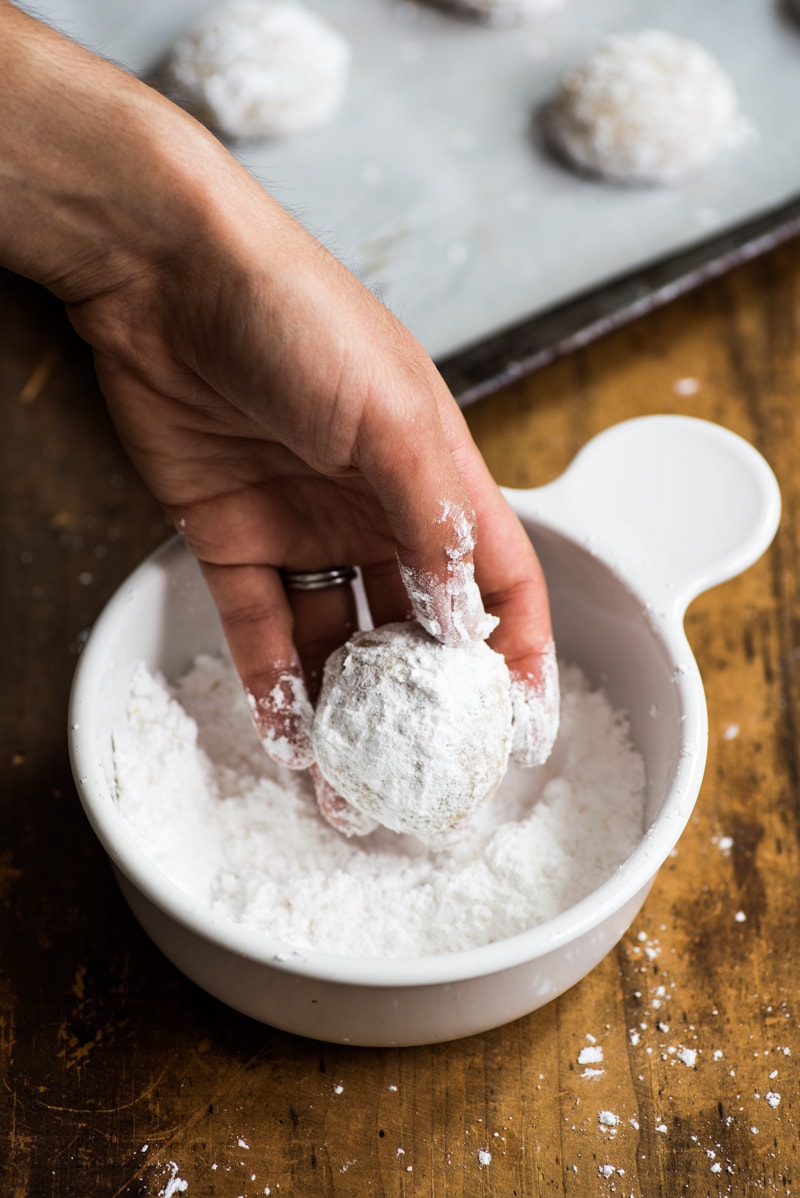 A bowl of powdered sugar with a mexican wedding cookie.