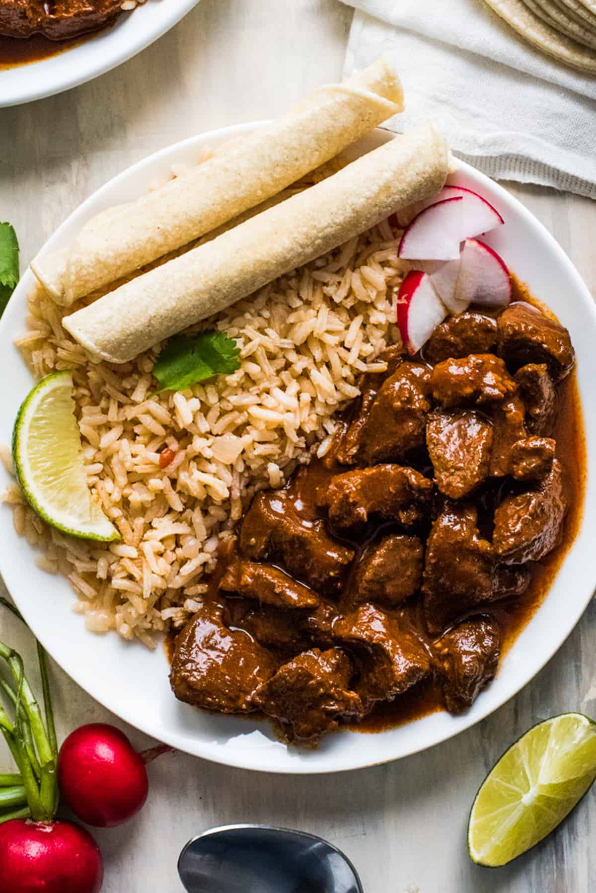 Chile colorado on a plate with mexican rice and corn tortillas.
