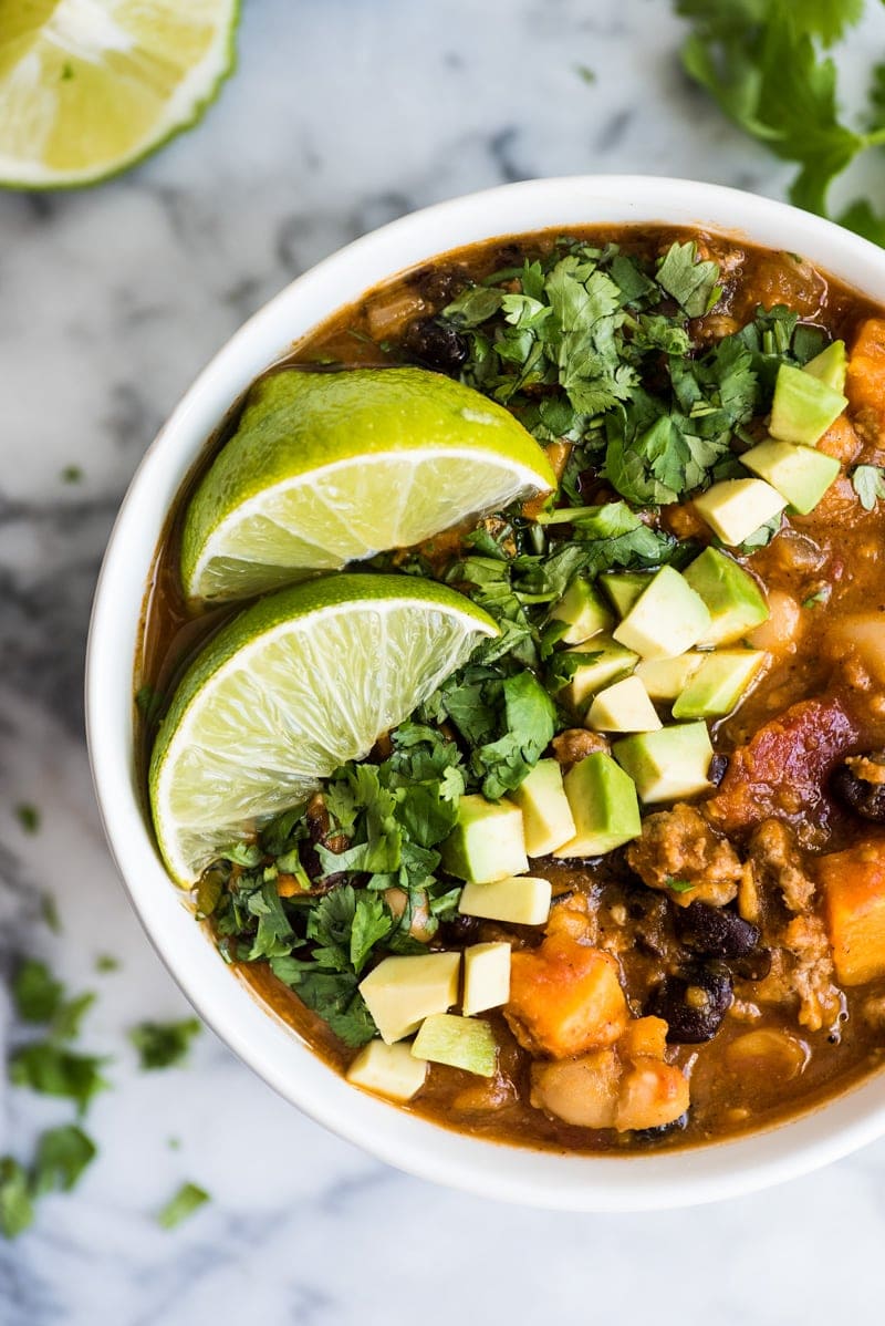 Turkey pumpkin chili in a bowl with lime wedges, cilantro and avocados.