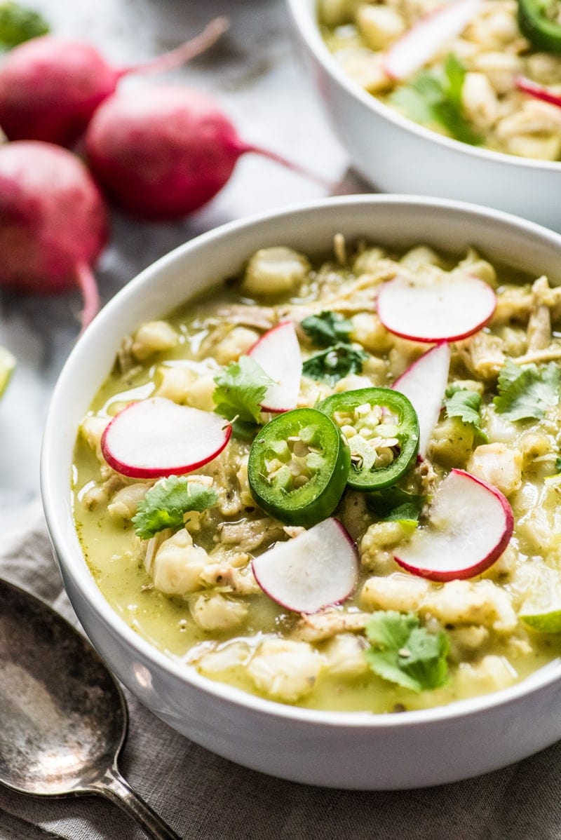 Pozole verde in a white bowl topped with cilantro, radishes and jalapeno slices.
