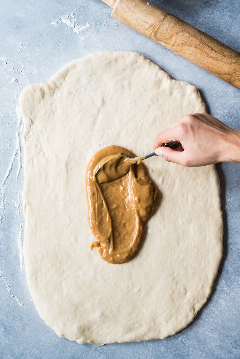 A hand spreading dulce de leche on dough