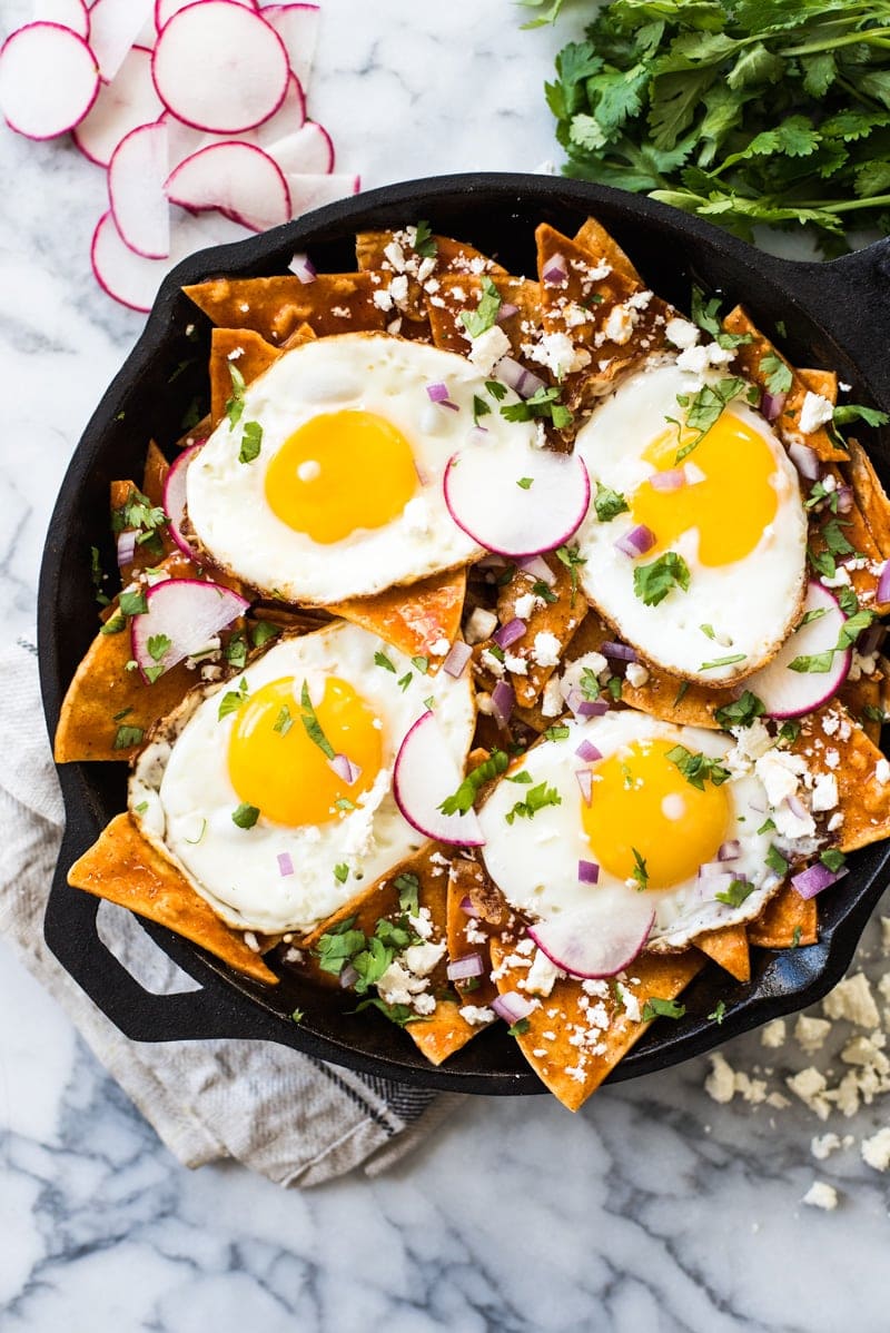 Red chilaquiles topped with sunny side up eggs in a black cast iron skillet.