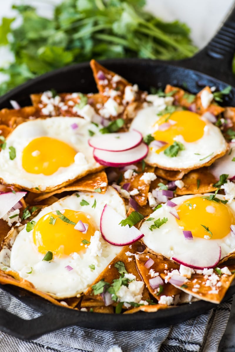 Sunny side up eggs on top of red chilaquiles in a black cast iron skillet.