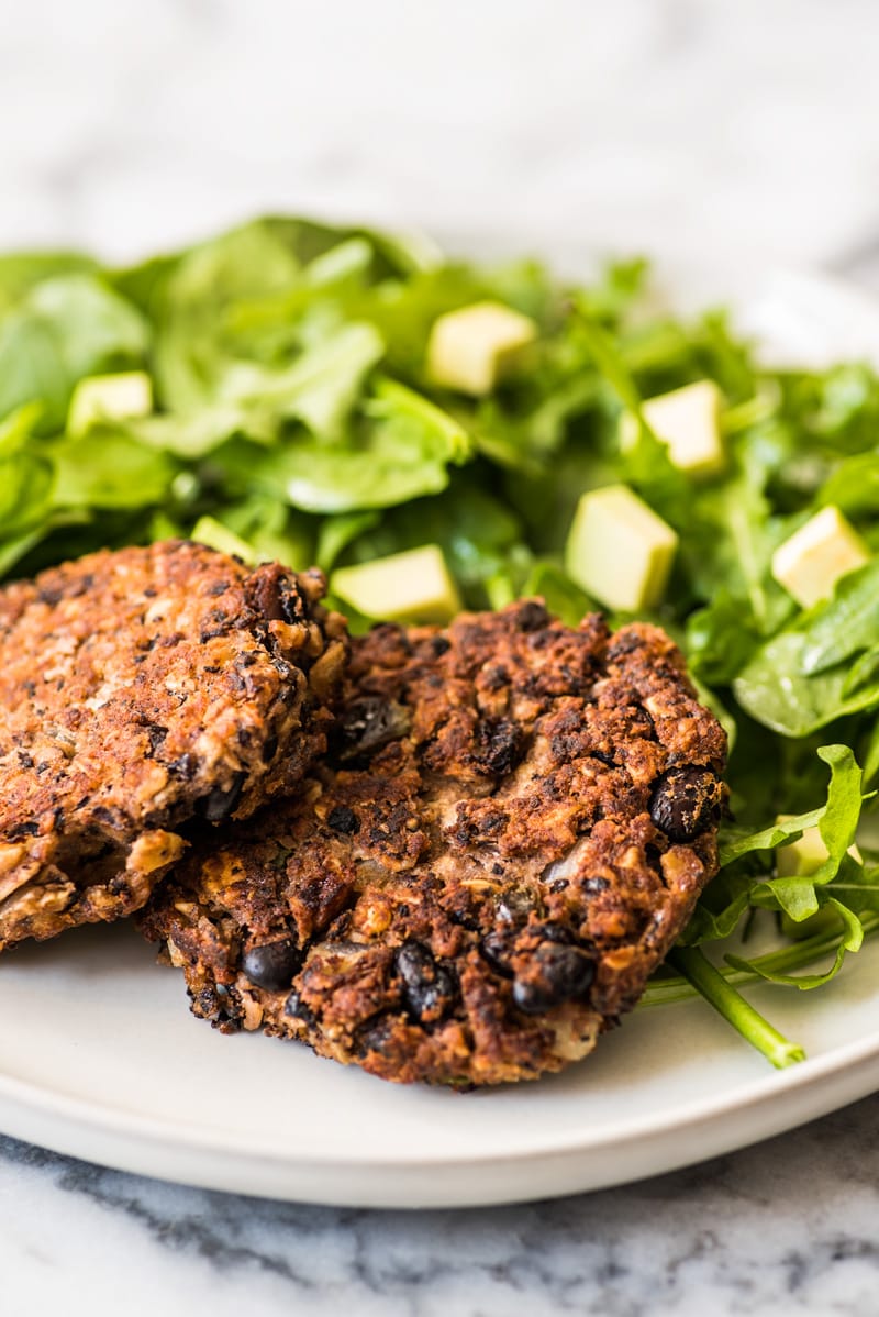 Two black bean patties on a plate with greens.