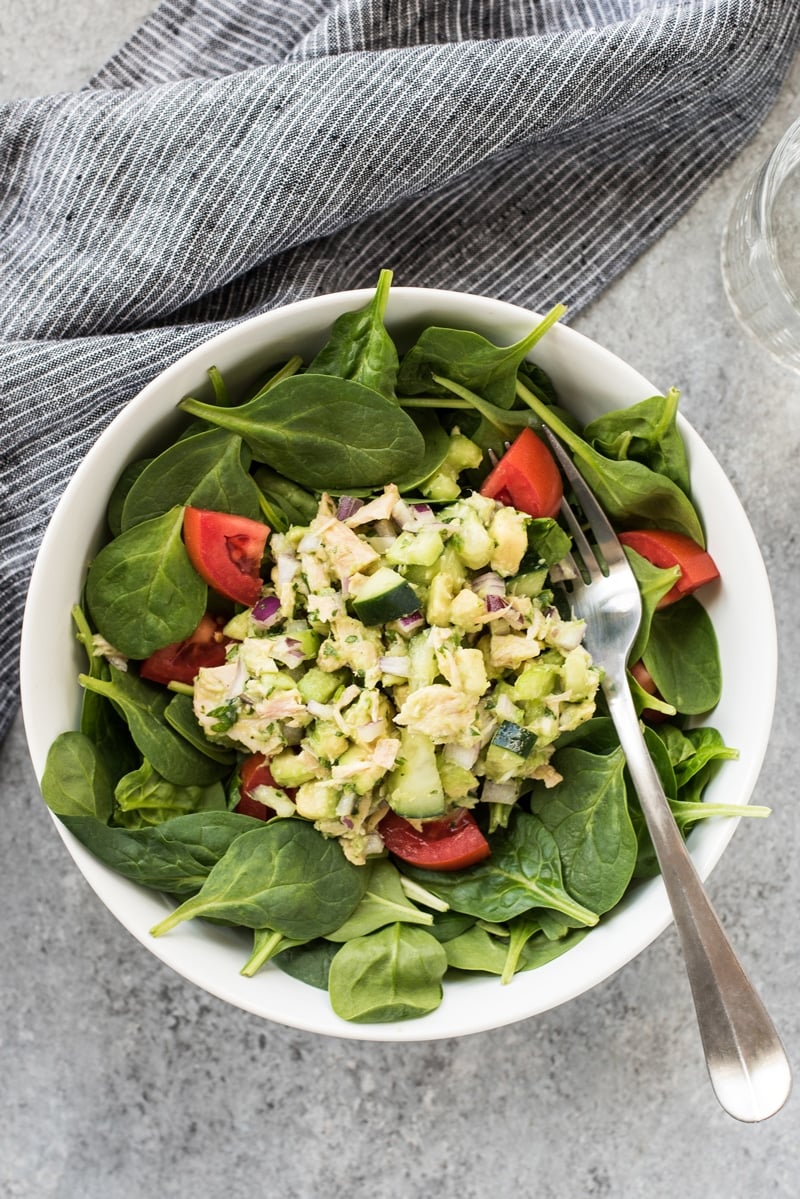 Avocado tuna salad in a white bowl with fresh spinach leaves.