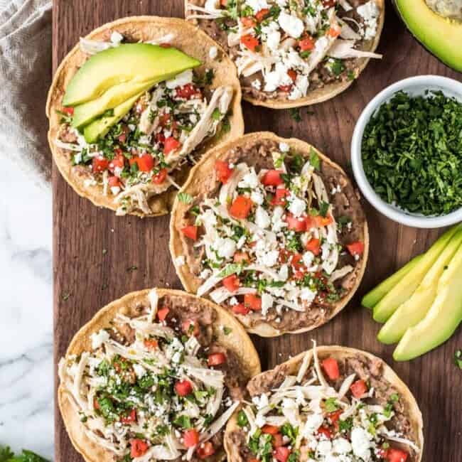 These crispy and crunch Slow Cooker Salsa Verde Chicken Tostadas are topped with a layer of delicious refried beans, salsa verde chicken, tomatoes, cilantro queso fresco and avocados.