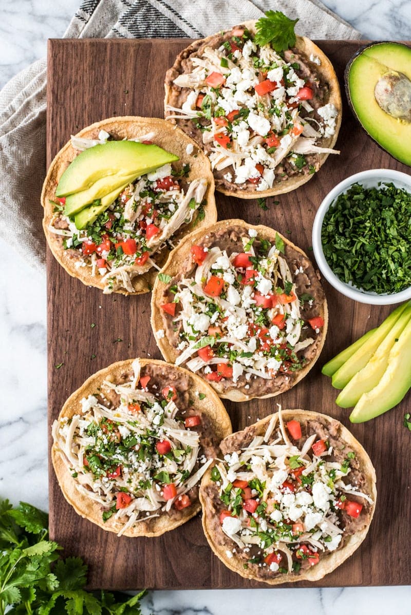 These crispy and crunchy Slow Cooker Salsa Verde Chicken Tostadas are topped with a layer of delicious refried beans, salsa verde chicken, tomatoes, cilantro, queso fresco and avocados.