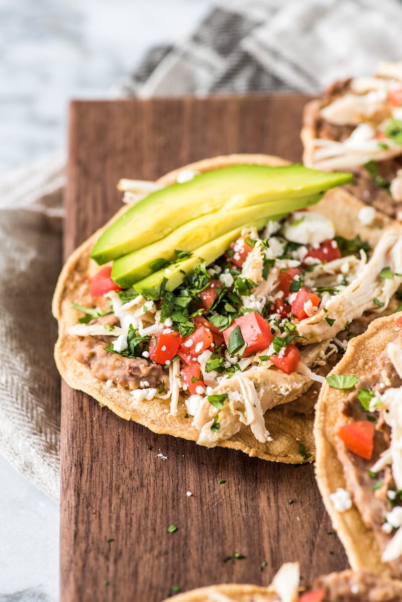 These crispy and crunchy Slow Cooker Salsa Verde Chicken Tostadas are topped with a layer of delicious refried beans, salsa verde chicken, tomatoes, cilantro, queso fresco and avocados.