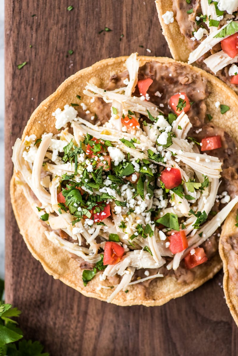 These crispy and crunchy Slow Cooker Salsa Verde Chicken Tostadas are topped with a layer of delicious refried beans, salsa verde chicken, tomatoes, cilantro, queso fresco and avocados.