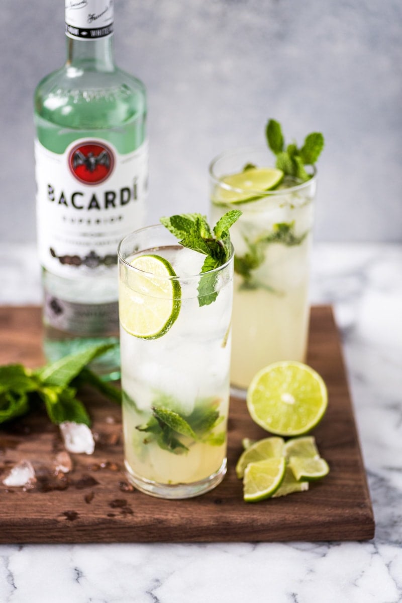 two glasses of mojitos with accompaniments surrounding it.