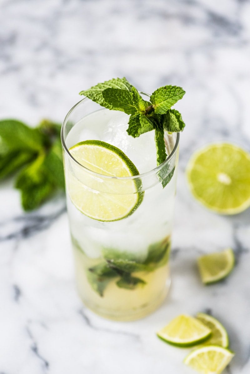 A mojito cocktail in a tall clear glass topped with mint leaves and limes.