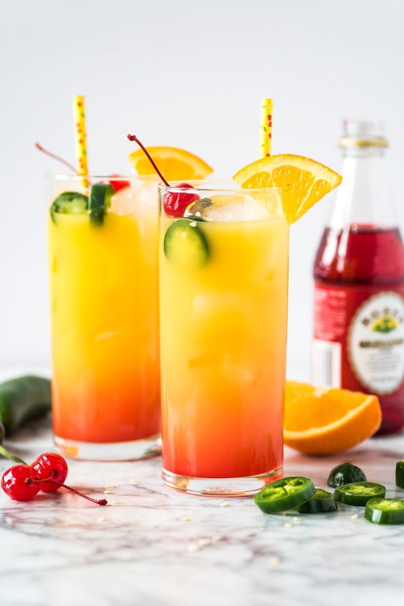 Tequila Sunrise cocktail in a glass topped with maraschino cherries and an orange slice.