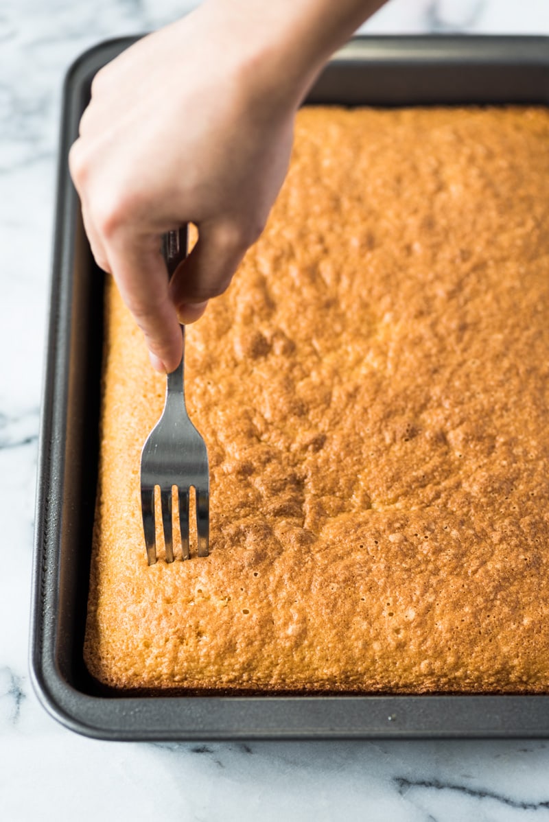Poking tres leches cake with a fork.