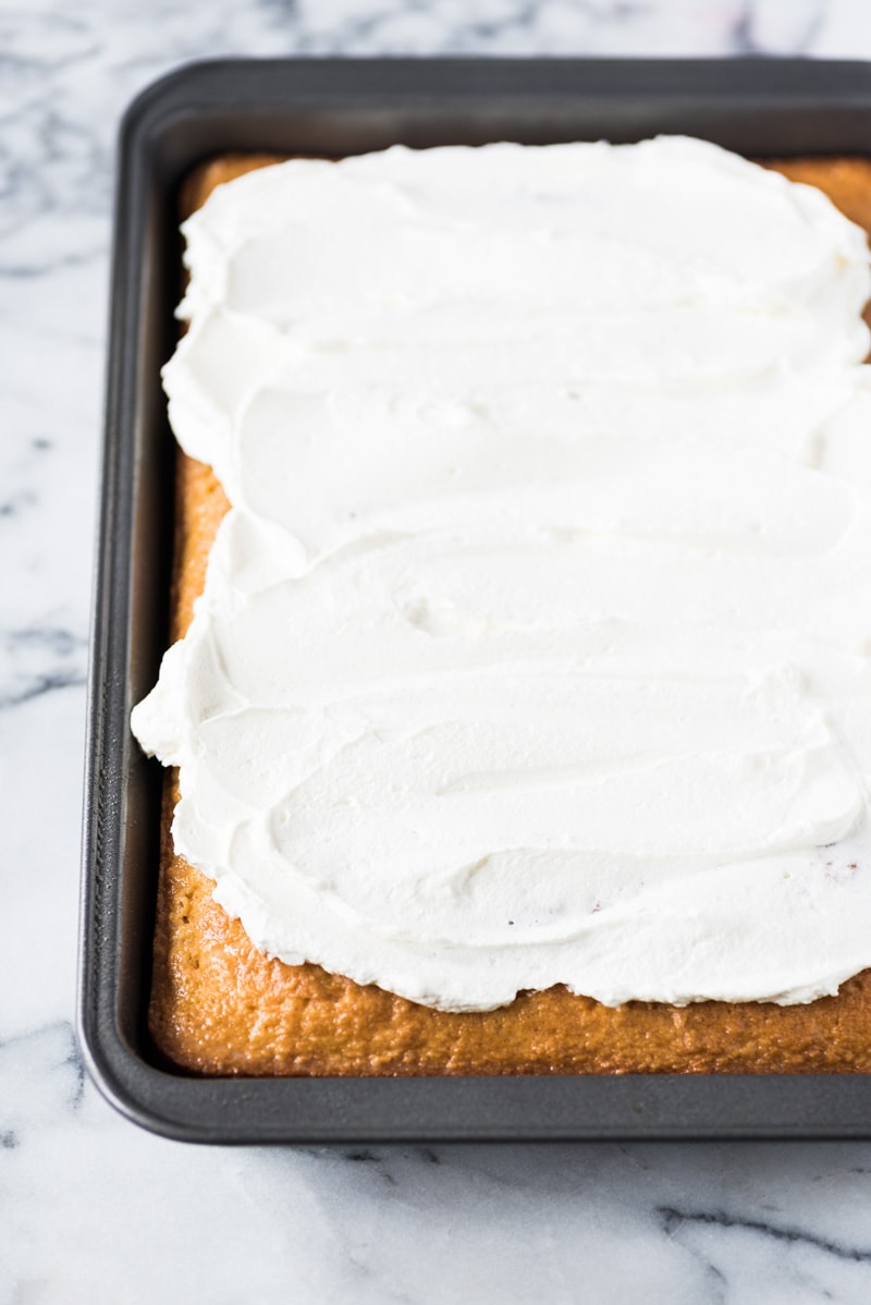Whipped cream topping spread over a tres leches cake in a pan.