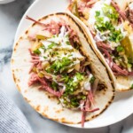 Slow cooker corned beef tacos in a flour tortilla topped with sauerkraut and sour cream.