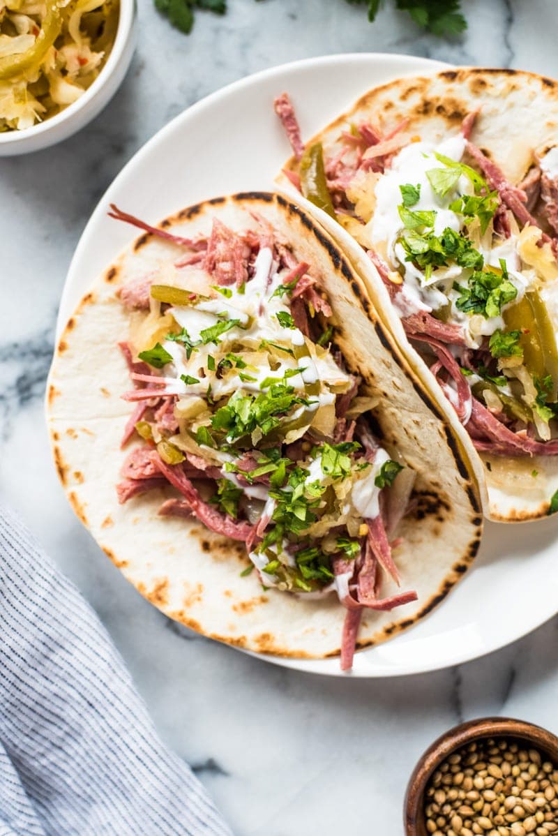 Slow cooker corned beef tacos in a flour tortilla topped with sauerkraut and sour cream.