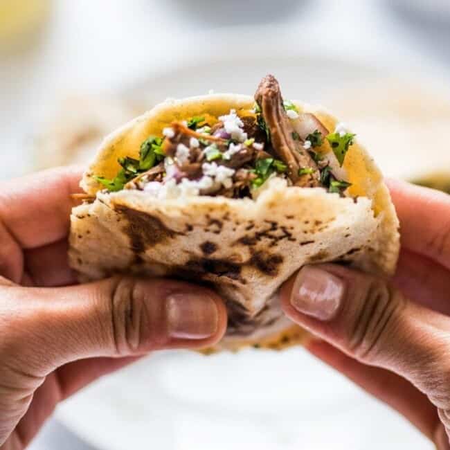 Two hands hold a gordita stuffed with meat and cheese.