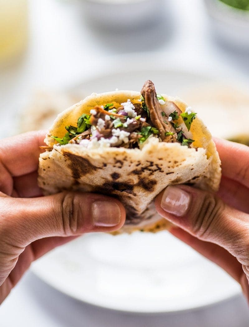 A hand holding a gordita stuffed with shredded beef, cheese and cilantro.