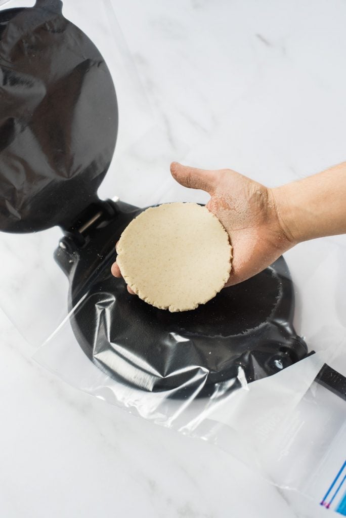 Hand removing freshly pressed raw masa dough for corn tortilla