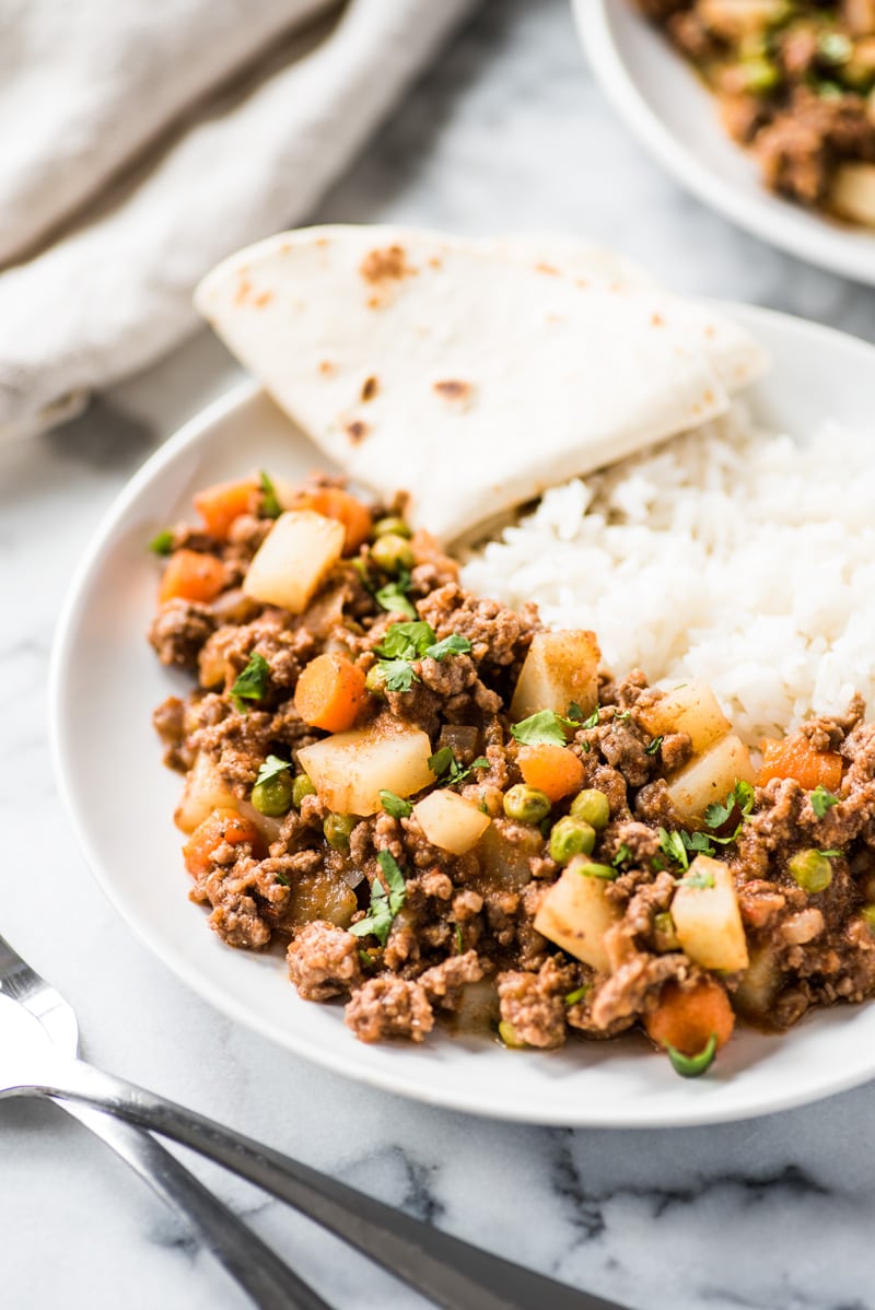 Mexican picadillo in a white bowl with rice and a flour tortilla