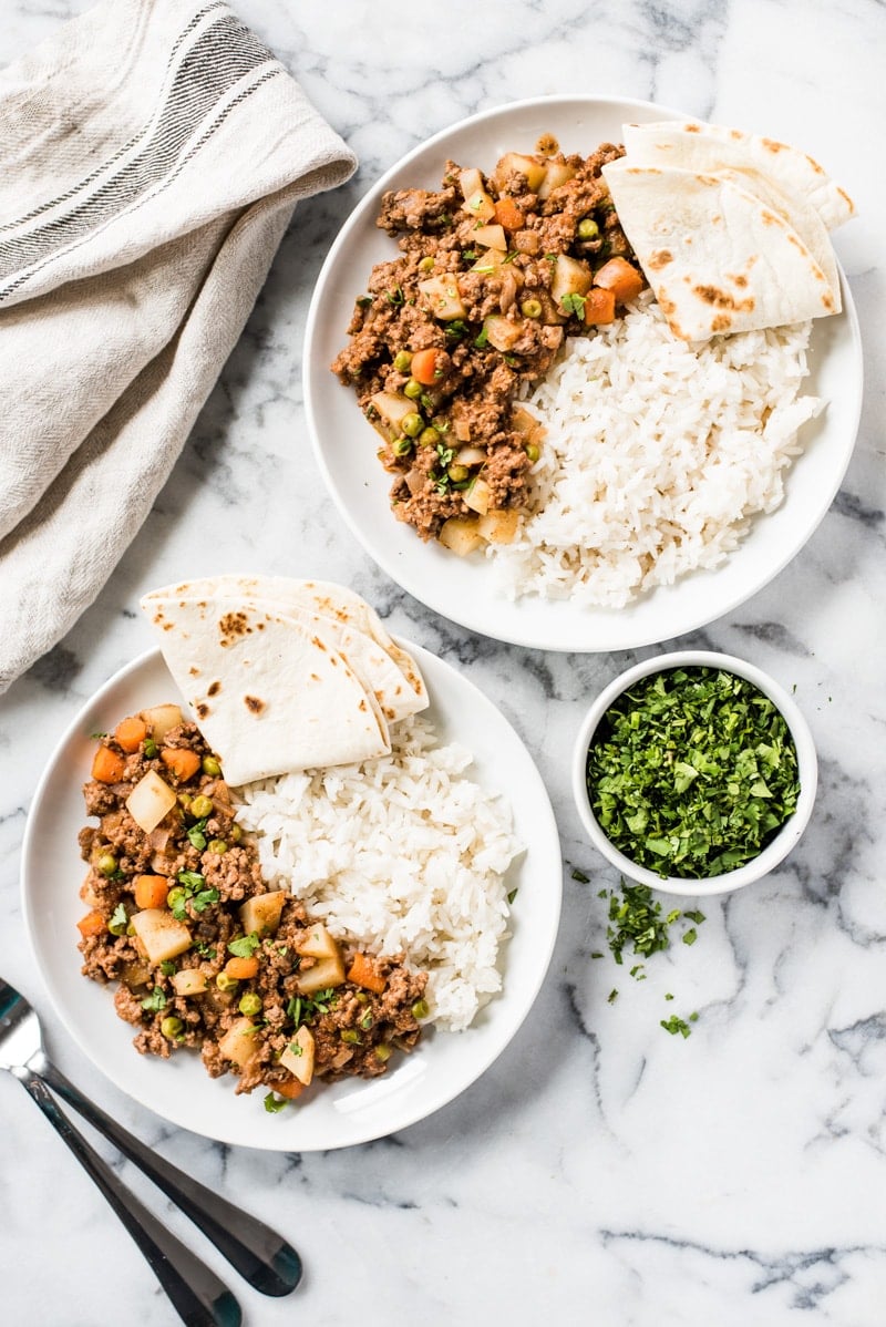 Two plates of picadillo recipe served with white rice, a flour tortilla and chopped cilantro.