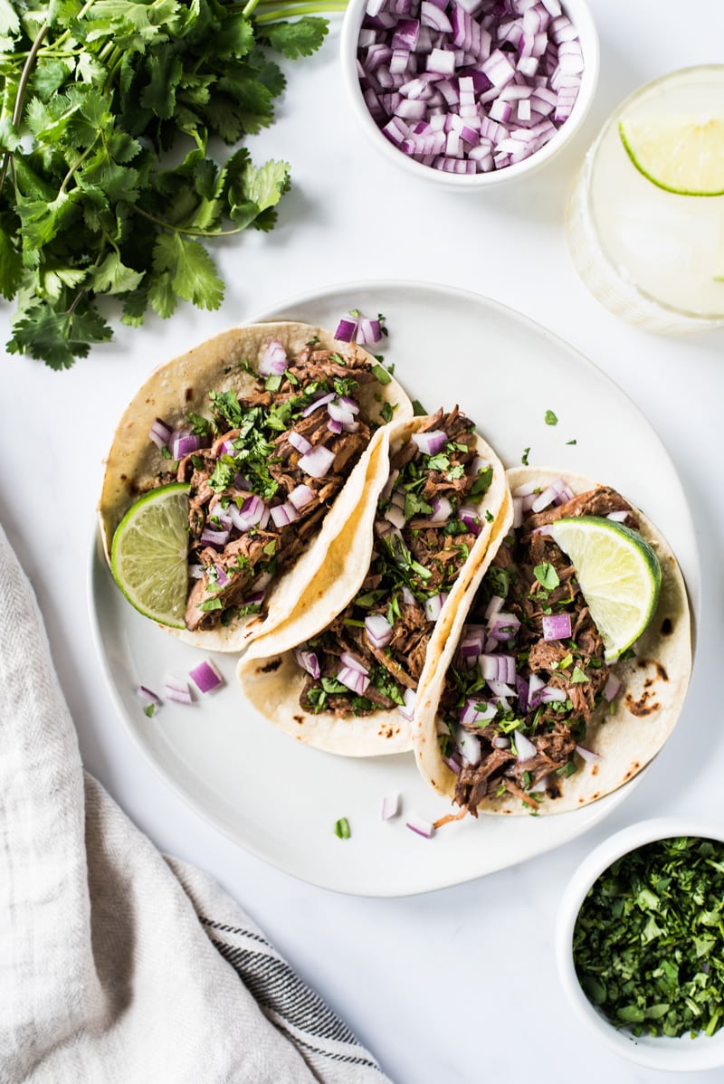 Barbacoa beef in tacos on a white plate.