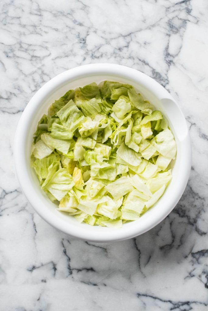 A white mixing bowl filled with chopped iceberg lettuce.