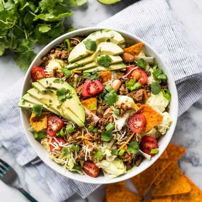 This Taco Salad recipe is the absolute best! Made with seasoned ground beef, chopped lettuce and all your favorite toppings (including nacho-flavored tortilla chips), this salad is ready in under 30 minutes and the kids will love it!