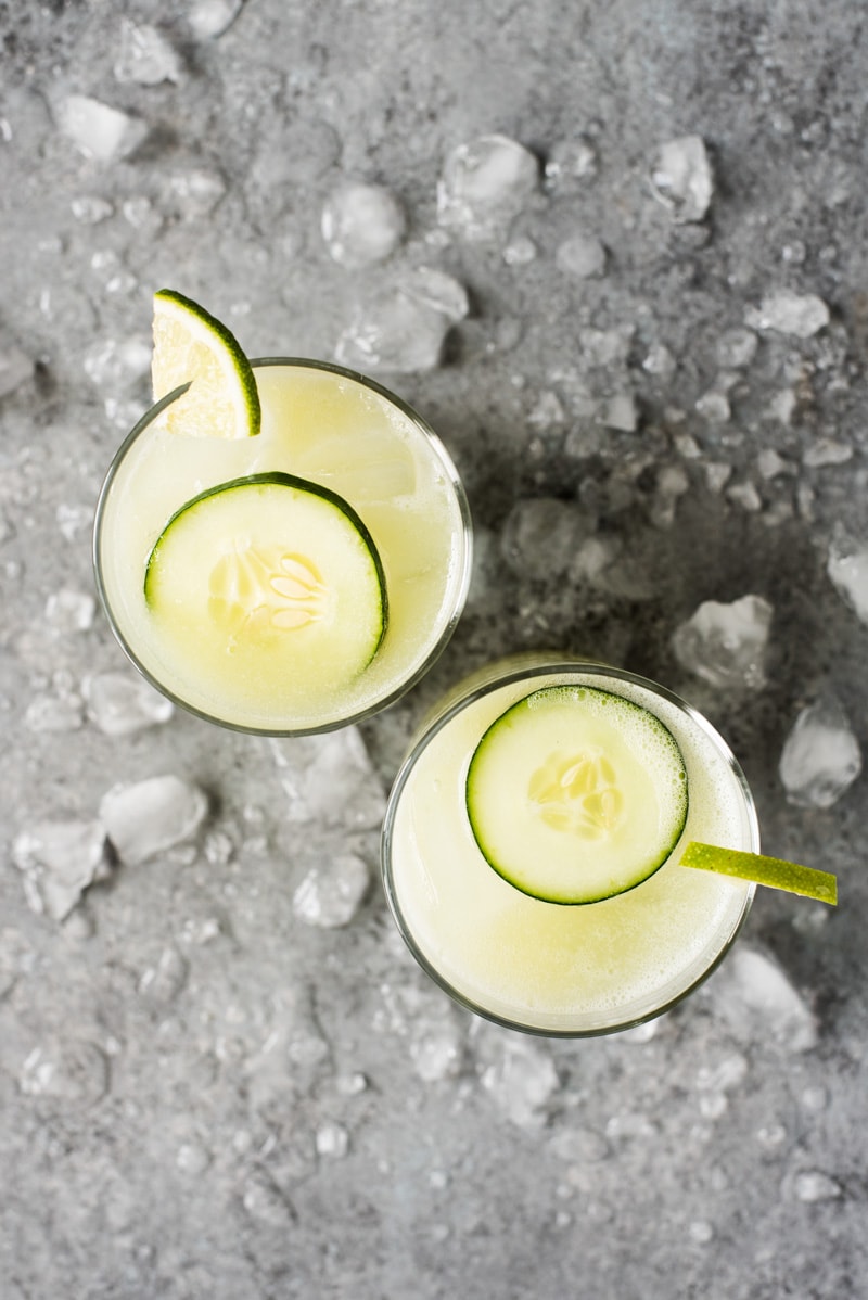 Cucumber water (agua fresca) in two glasses filled with ice and topped with freshly sliced cucumbers and lime wedges.