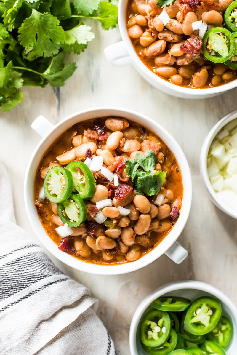 Charro beans (or frijoles charros) in a white bowl topped with jalapenos and cilantro.