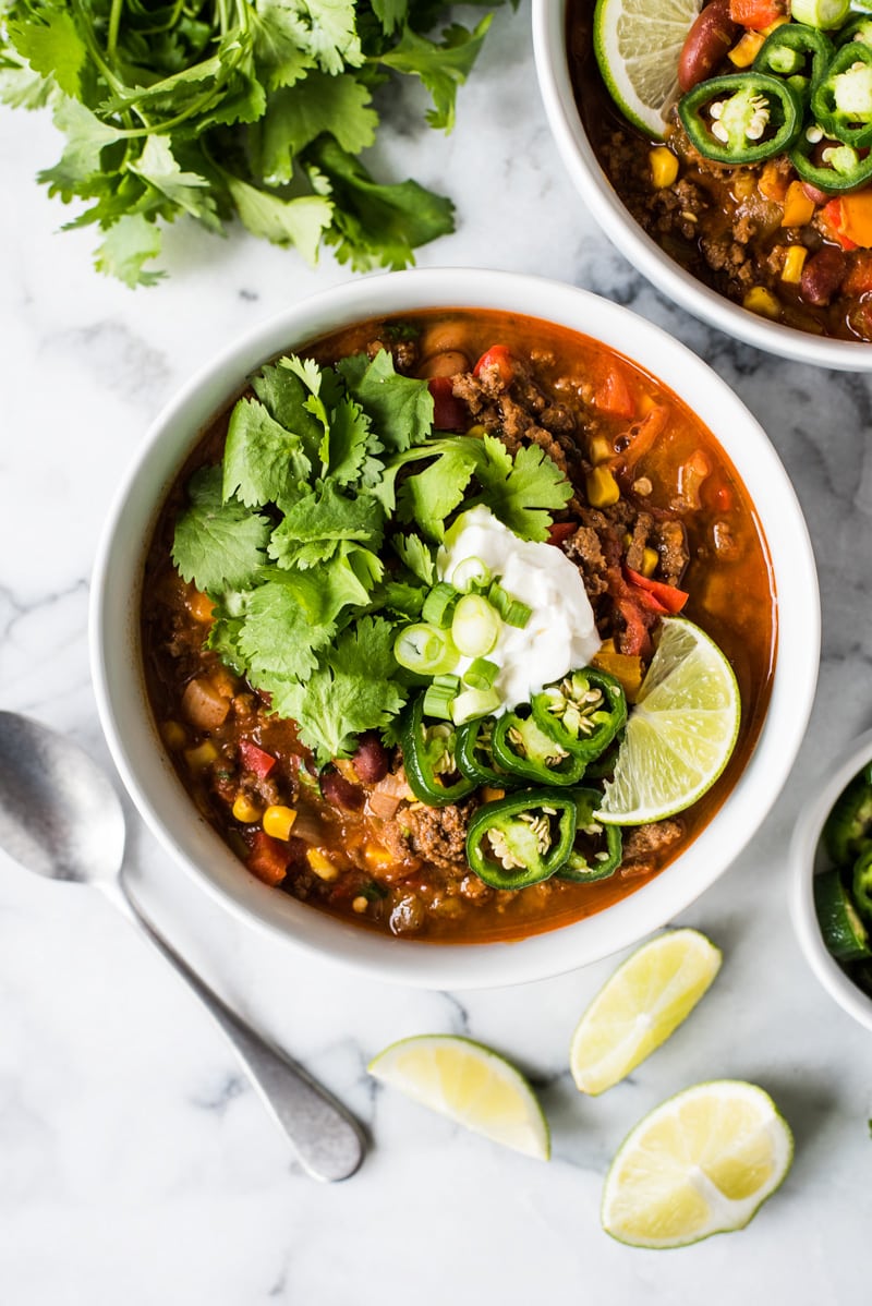 A bowl of taco soup with cilantro and sour cream on a white table.