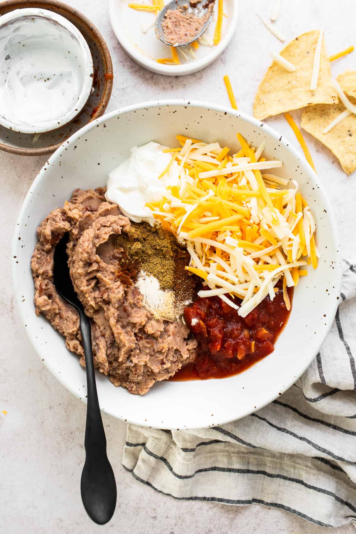 Refried beans, chunky salsa, shredded cheese, sour cream, and seasonings in a mixing bowl.