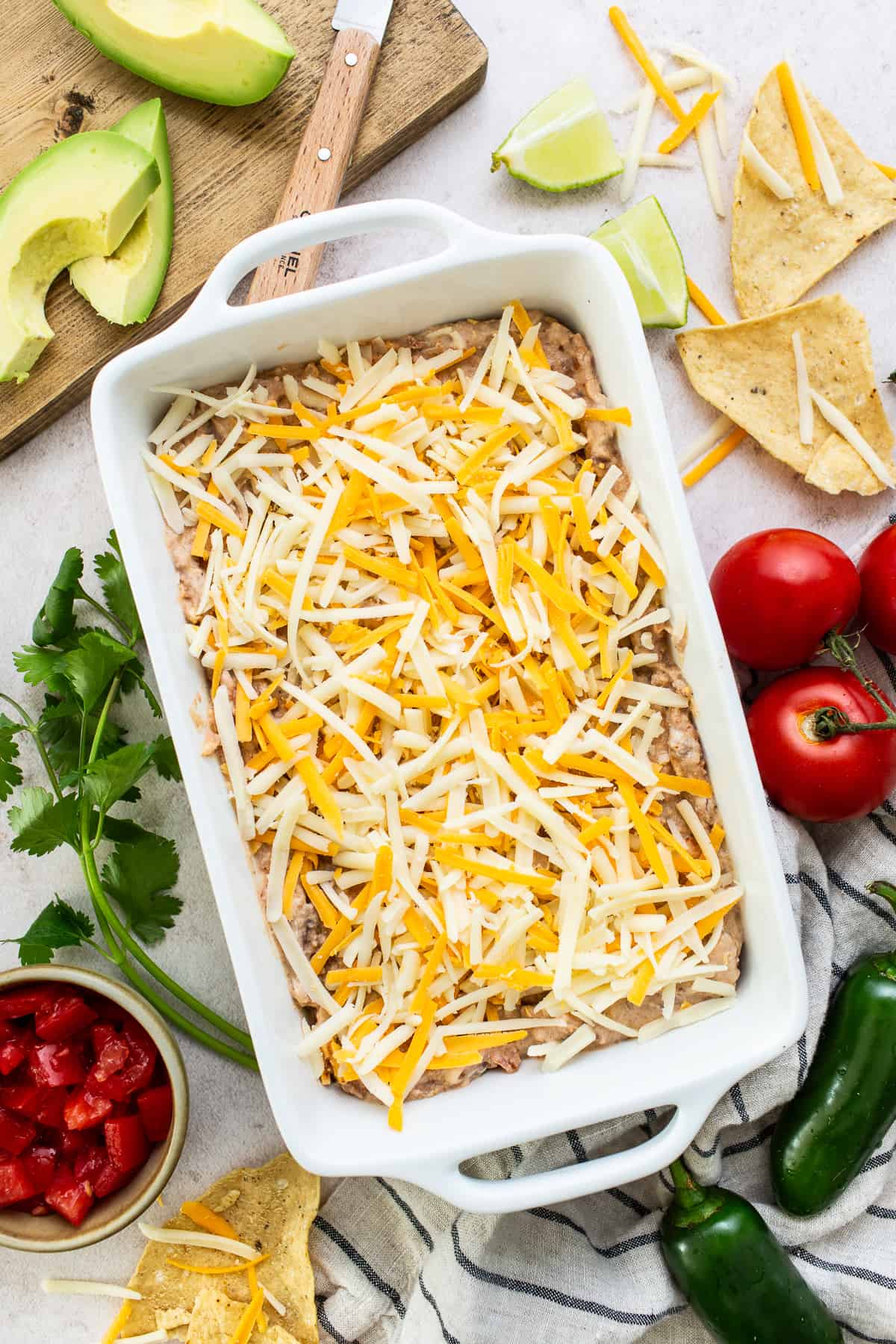 Shredded cheese on top of a baking dish of bean dip before being baked.