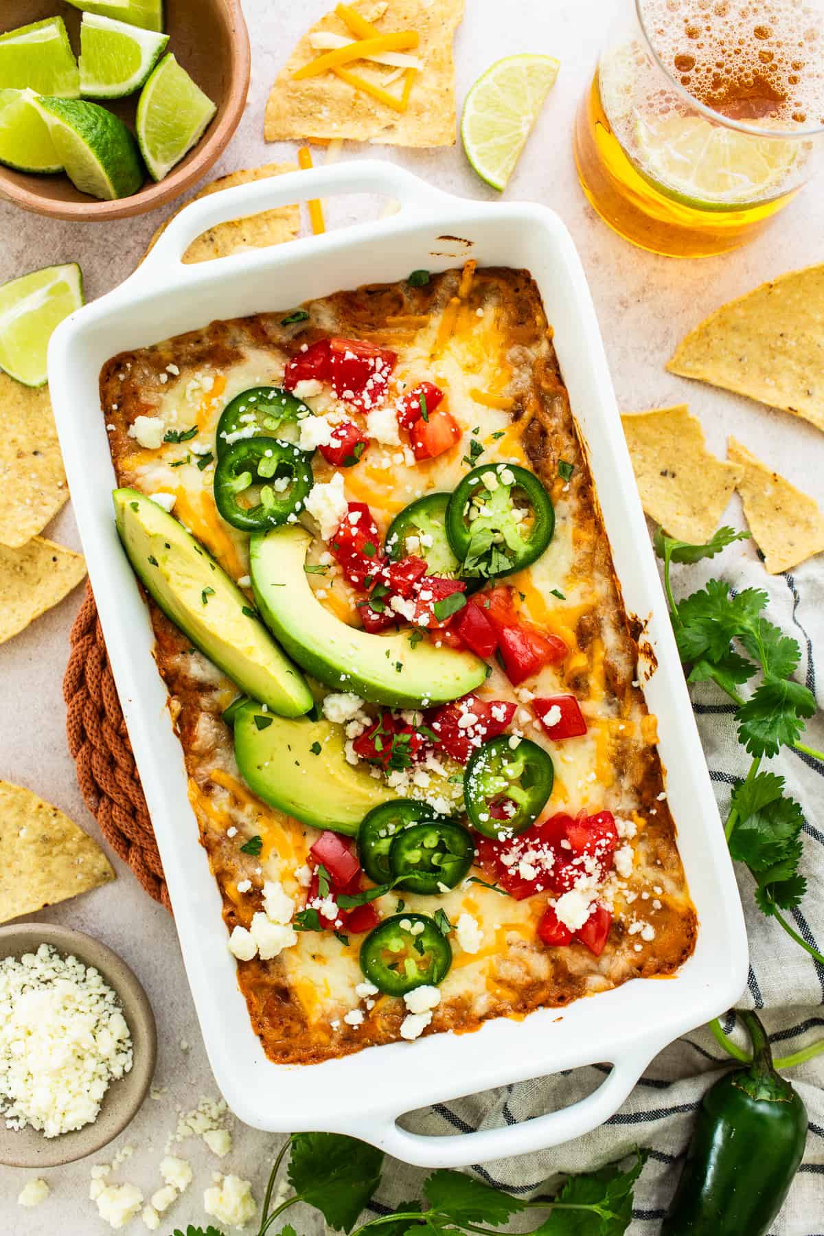 Bean dip topped with melted cheese and garnished with diced tomatoes, cotija cheese, sliced peppers, and avocados.