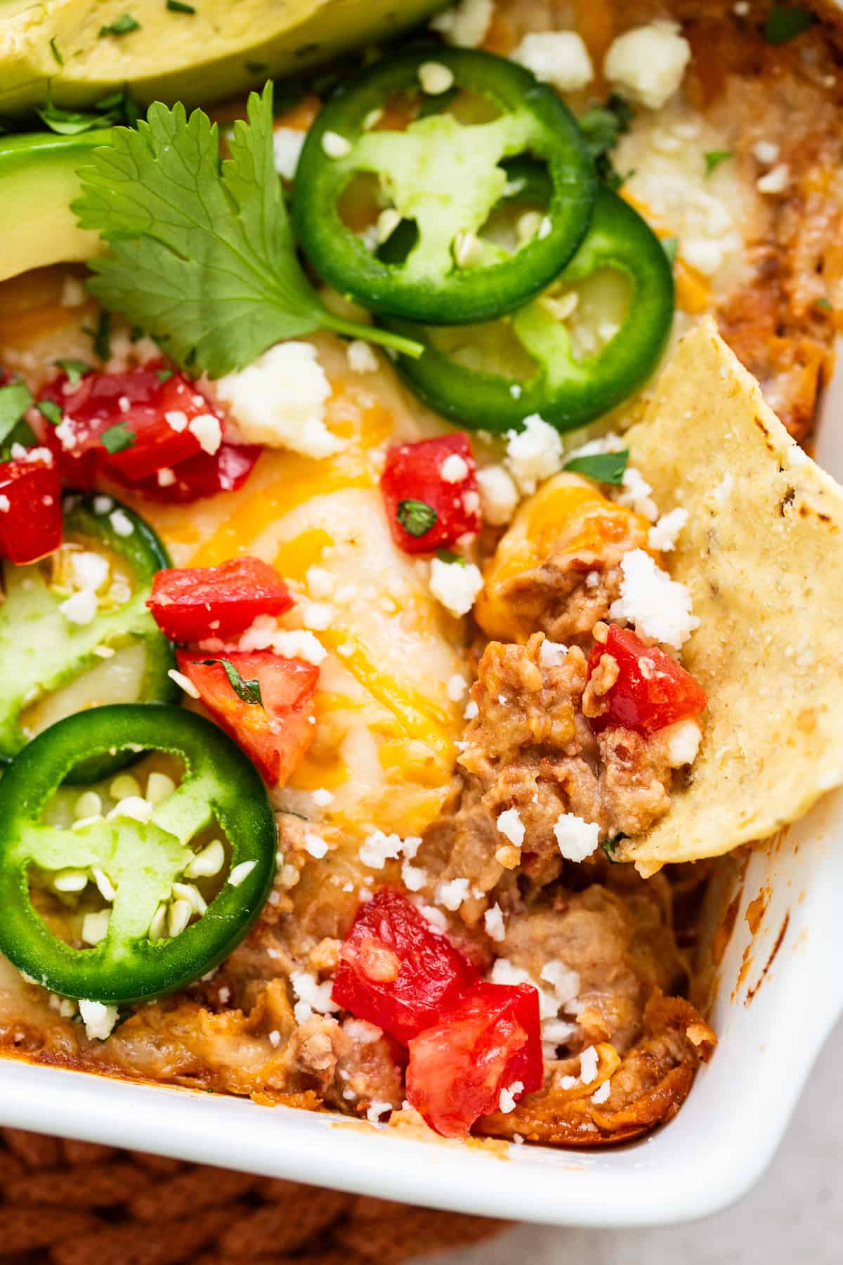 A tortilla chip dipped in a baking dish of hot and bubbly bean dip.