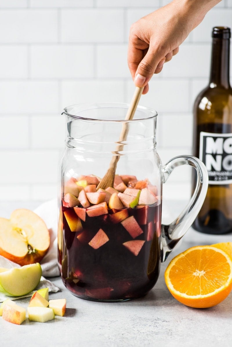 Red sangria in a glass pitcher being mixed with a spoon.