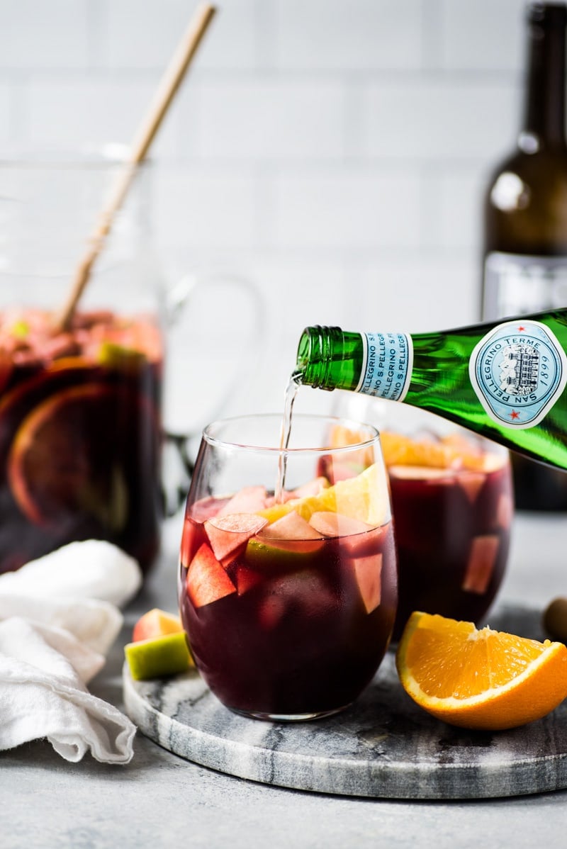 Sangria in a glass topped with chunks of fruit including oranges and apples.