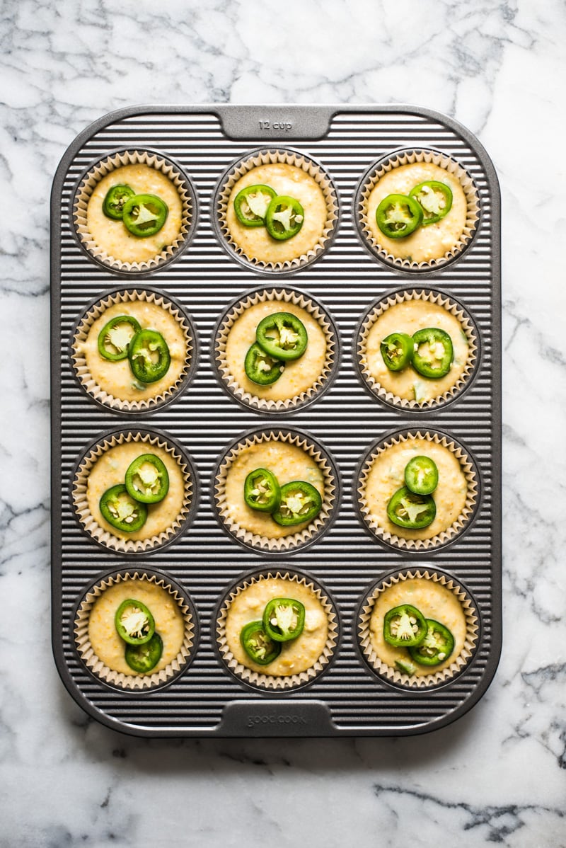 A large muffin tin filled with jalapeno cornbread batter.