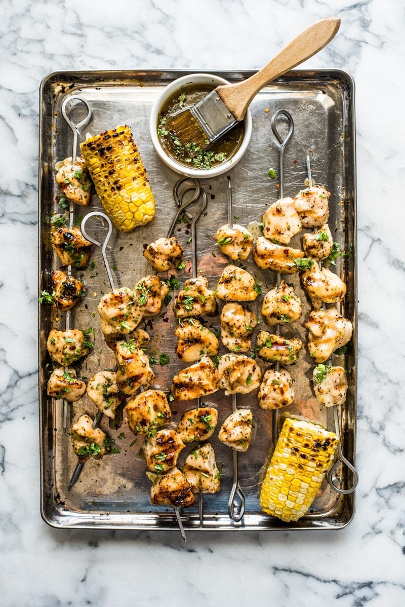 Grilled chicken kabobs on skewers on a metal baking sheet.
